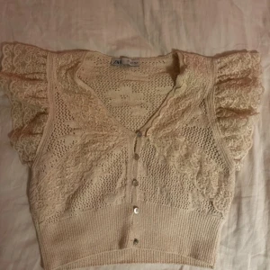 Beige spetsblus från Zara - Supersöt beige blus från Zara med v-ringning, knappar framtill och volangiga spetsärmar. 