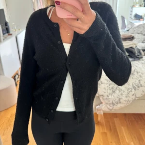 Svart kofta med knappar - Svart, klassisk kofta med rund hals och knäppning framtill. Långärmad och ribbad vid muddar och hals. Enkel och stilren, passar till allt.