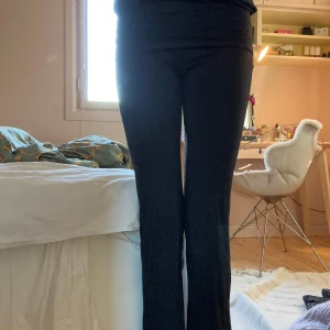 Svarta yogapants byxor från Gina Tricot - Svarta yogapants byxor från Gina Tricot med låg/normalhög  midja. Byxorna är i stretchigt och mjukt material som sitter skönt och har en snygg passform. Perfekta för dig som gillar en klassisk look med lite utsvängda ben. Byxorna är lite dammiga/luddiga men det går säkert att få bort. Skriv gärna vid frågor! 