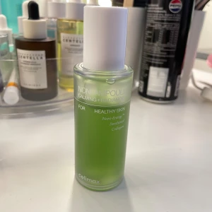 Celimax Noni Ampoule Calming + Radiance - Celimax Noni Ampoule Calming + Radiance är ett ansiktsserum i en frostad glasflaska med vit kork. Innehållet är grönt och formulan är berikad med noni-extrakt, panthenol och kollagen för att lugna och ge glow till huden.