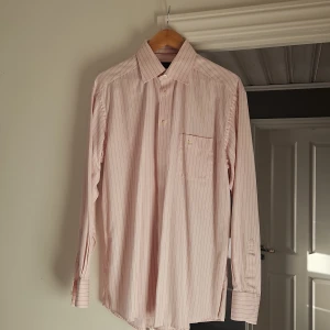 Ljusrosa randig skjorta från Eton - Snygg ljusrosa skjorta från Eton med tunna vertikala ränder i mörkare nyans. Klassisk krage, bröstficka och knäppning framtill. Tillverkad i bomull och passar perfekt för en clean och stilren look.