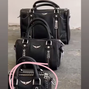 Svart handväska Zadig & Voltaire skinn - Cool svart handväska från Zadig & Voltaire i äkta skinn med silverfärgade metalldetaljer och dragkedjor. Väskan har dubbla handtag, avtagbar axelrem och ikonisk vinge framtill. Dekorativa nitar längs kanterna ger en edgy vibe.