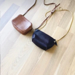 Väsk packet  - Säljer två stilrena axelväskor. Den ena är svart med guldfärgad kedja och slät yta, den andra är brun med fyrkantig form och präglat mönster som påminner om ormskinn. Båda har dragkedja och justerbara axelremmar. Perfekta för att bära det viktigaste. Den bruna har tappat lite färg men är väldigt vacker.