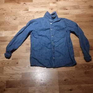 Jeansskjorta från D.M.D. - Klassisk blå jeansskjorta från D.M.D. by denim day med bröstficka och knappar framtill. Skjortan har lång ärm och är tillverkad i mjukt jeanstyg som ger en avslappnad vibe, använt typ 3 gånger och gillar inte dem så mycket