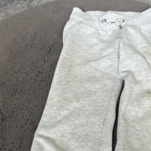 Grå mjukisbyxor från Gina Tricot - Snygga ljusgrå mjukisbyxor från Gina Tricot i storlek 134/140. Byxorna har ribbad midja med snörning och är tillverkade i mjukt bomullsmaterial. Perfekta för chill dagar och har en klassisk, rak passform. använt ganska många gånger men funkar jättebra. ser lite bred ut på bilden men annars är de bra lite större än storleken som står