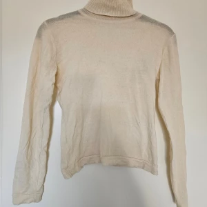 Varmvit polotröja i cashmere - Klassisk polotröja med lång ärm och ribbad krage. Tröjan är i mjuk cashmere som är både värmande och skönt. Fint skick, lagad bak i kragen. Litet hål på framsidan som kanppt syns