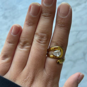 Guldfärgad ring med droppformad sten - Snygg guldfärgad ring med en unik, böjd form och en stor droppformad klar sten i mitten.