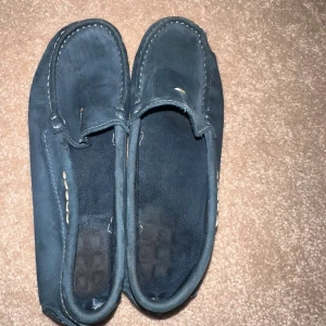 Mörkblå mockaloafers med gummisula - Snygga mörkblå loafers i mocka med klassisk söm runt tån och ljusbrun gummisula med mönstrat grepp. Skorna har en stilren och enkel design som passar till många outfits. Perfekta för dig som gillar en avslappnad men ändå uppklädd look. Jag vet inte märket. 