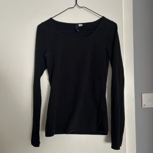 Svart långärmad topp - Säljer en svart långärmad topp med rund halsringning från HM. Tröjan är i storlek 36/S, har längre ärmar och är lång i längden.