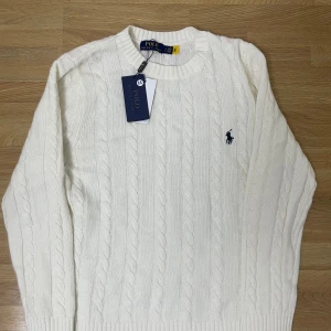 Vit kabelstickad tröja ganska tunn Polo Ralph Lauren (Dm innan du köper) - Tunn Kabelstickad vit tröja från Polo Ralph Lauren med klassisk rund halsringning och broderad marinblå logga på bröstet. Tröjan har ribbade muddar och är långärmad, perfekt för lager-på-lager under kyliga dagar.
