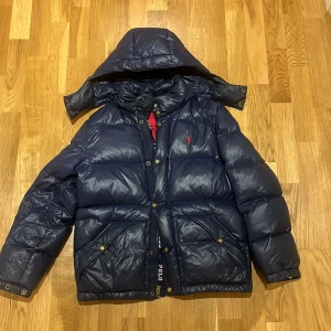 Mörkblå dunjacka från Polo Ralph Lauren - Snygg mörkblå dunjacka från Polo Ralph Lauren med röd broderad logga på bröstet. Storleken uppskattar jag till S men passar även mindre och något större!! Skicket är superbra❤️❤️