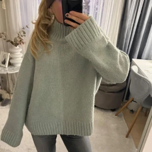 Ljusgrön stickad polotröja oversized - Supermysig ljusgrön stickad polotröja med oversized passform och breda ribbade muddar vid ärmslut och nederkant. Hög krage som ger extra värme och chill vibe. Perfekt att slänga på sig när det är kallt ute.
