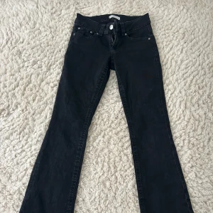 Svarta bootcut jeans med fickdetaljer - Svarta jeans med bootcut passform. Baktill finns två fickor med lock och silverfärgade knappar. Jeansen har normal midja.