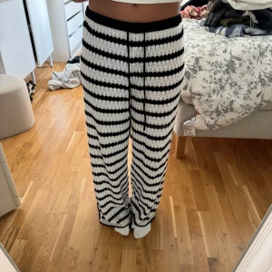 Randiga stickade byxor med snörning - Säljer ett par stickade byxor med svartvita ränder och snörning i midjan. Byxorna har en loose och wide passform, perfekt för en chill och avslappnad look. Materialet är mjukt och stretchigt, vilket gör dem superbekväma att ha på sig.