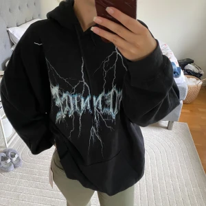 Svart oversized hoodie med blixttryck - Cool svart hoodie med stort tryck av vita och blå blixtar framtill. Oversized passform, huva med snörning och stor magficka. Perfekt för dig som gillar streetstyle och vill sticka ut med en edgy look.