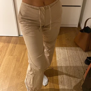 Beiga byxor med snörning Gina Tricot XS - Säljer ett par beiga byxor från Gina Tricot i storlek XS. Byxorna har resår i midjan med snörning, raka ben och en bakficka med lock. (Jag är 177cm)
