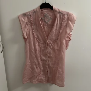 Ljusrosa blus från edc  - Supersöt ljusrosa blus från edc med volangdetaljer och knappar framtill. Ärmlös modell med fina veckade detaljer både fram och bak. Perfekt för dig som gillar romantisk och feminin stil.