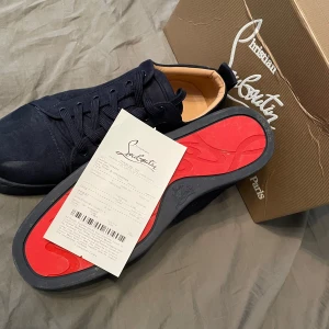 Mörkblå sneakers från Christian Louboutin - Säljer ett par mörkblå sneakers från Christian Louboutin i mocka med klassisk röd sula. Skorna har snörning och rund tå, och är riktigt snygga till både jeans och chinos. Kommer med originalkartong och äkthetsbevis.