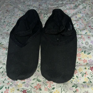 Svarta balettskor - Svarta balettskor i tyg med korsade resårband över foten för extra stöd. Skorna har en mjuk och flexibel sula, perfekt för dans eller gymnastik. Klassisk design med rund tå och låg profil som ger en smidig känsla på golvet. Säljer då jag ej dansar balett längre, skorna är använda två gånger🙂✨