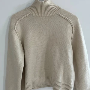 Stickad tröja - Supervacker, elegant och trendig beige stickad tröja med hög krage och fina detaljer! Har en liten (knappt synlig, se sista bilden) sminkfläck vid kragen, därav säljs den billigare 🩷