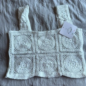 Vit virkad linnetopp från Rinboo - Superfin vit virkad linnetopp från Rinboo med breda axelband och fyrkantig halsringning. Toppen har ett unikt mönster av virkade cirklar och rutor, vilket ger en bohemisk och somrig vibe. Perfekt till jeans eller kjol för en chill look.