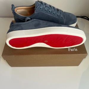Blå Christian Louboutin sneakers mocka - Snygga blå sneakers från Christian Louboutin i mjuk mocka med klassisk röd sula och vita kanter. Skorna har rund tå, snörning och beige innersida i skinn. Kommer med originalkartong och tre dustbags.Perfekt för dig som gillar exklusiva detaljer och stilren design. Priset kan sänkas vid snabb affär😊