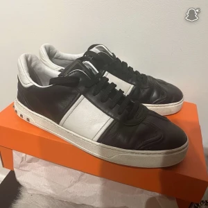 Valentino Garavani svartvita sneakers - Svartvita Valentino Garavani sneakers i skinn med klassisk snörning och ikoniska nitar på sulan. Snygg kontrast mellan svart och vitt, samt diskret logga på plösen. Perfekta för dig som vill ha en lyxig och edgy look till vardags. Pasar