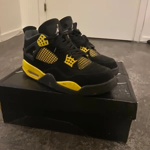 Nike Air Jordan 4 Retro yellow thunder - Säljer ett par Nike Air Jordan 4 Retro i svart och gul. Skorna har coola meshdetaljer, snörning och den klassiska Jumpman-loggan på plösen. Ovandelen är i mocka och syntet, med kontrasterande gula inslag och svart sula. Perfekta för dig som vill sticka ut med din sneakerstil.
