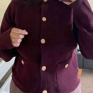 Vinröd kofta med guldknappar - Säljer min kofta helt ny har inte använt den. En vinröd Stickad kofta med snygga guldknappar framtill och på fickorna. Materialet är mjukt och ger en lyxig känsla perfekt för hösten🍂✨🐻🤎Skriv om ni har frågor💞