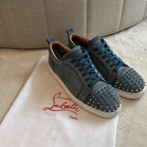  Christian Louboutin - Snygga blå sneakers från Christian Louboutin i mocka med coola silverfärgade nitar på tån. Skorna har blå snörning, vit sula och en klassisk rund tå. Perfekta för dig som vill sticka ut med en edgy och lyxig stil. 1 spik saknas samt inget og medföljer där av priset!