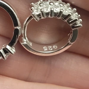  Helt nya Glittriga silverörhängen 925 -  Helt nya Säljer ett par snygga örhängen i äkta 925 silver med glittriga stenar i rad på framsidan. De är små, runda hoops med cool detalj av små silverkulor runt stenarna. Perfekt för dig som gillar bling och vill ha något som syns!