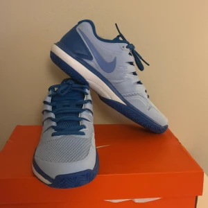 Träningskor från Nike - Snygga Nike träningsskor i två nyanser av blått med vit sula och klassisk swoosh på sidan. Skorna har mesh och syntetmaterial för bra andningsförmåga och komfort. Storlek 41. Helt nya och oanvända. Originalkartongen medföljer. 