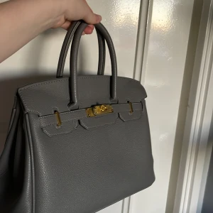 Grå väska  - Säljer en väska i grått Togo läder som inte används. Den har även plasten kvar på guld detaljerna 