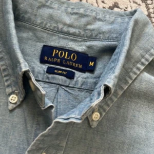 Ljusblå skjorta från Polo Ralph Lauren - Snygg ljusblå skjorta från Polo Ralph Lauren i slim fit-modell. Skjortan har klassisk krage, knäppning framtill och långa ärmar. Tillverkad i mjuk bomull och prydd med den ikoniska broderade loggan på bröstet.