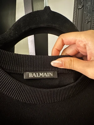 Svart stickad tröja Balmain Paris - Säljer min mans svarta stickad tröja från Balmain Paris med rund hals och lång ärm. Snyggt Balmain-märke på bröstet och stor vit logotyp längs ena ärmen. Storlek M. Priset kan diskuteras.