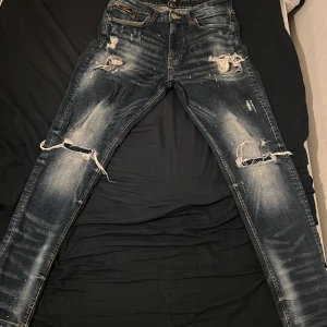 Blå slitna jeans med hål och slim fit  - Snygga blå jeans med slitningar och stora hål på knäna, samt distressed detaljer och blekta partier. Skinny fit med fem fickor och klassisk jeanslook. Perfekt för dig som gillar en edgy och trendig stil.