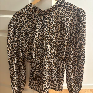 Leopardmönstrad blus från Boohoo - Säljer en snygg leopardmönstrad blus från Boohoo i storlek 36. Blusen har lång ärm, markerad midja och v-ringning med liten slits framtill. Färgerna är beige, svart och brun. Materialet är lätt och känns som polyester. Perfekt för dig som vill sticka ut med djurmönster.