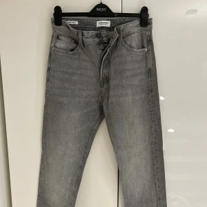 Grå jeans från Jack & Jones - Snygga grå jeans från Jack & Jones med relaxed passform och raka ben. Modellen heter Chris och har klassisk femficksdesign, knappgylf och subtila sömdetaljer på bakfickorna. Perfekt för dig som gillar en chill och stilren look.