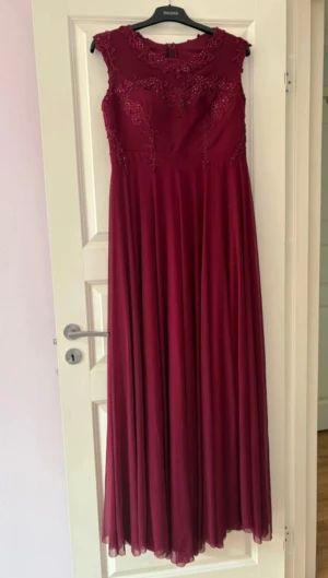 Vinröd långklänning med spetsdetaljer - Säljer en elegant vinröd långklänning med vackra spetsdetaljer och broderier upptill. Klänningen har ärmlös design och ett flytande, svepande tyg som ger en riktigt drömmig känsla. Perfekt för bal eller fest! Dragkedja i ryggen för enkel påklädning.