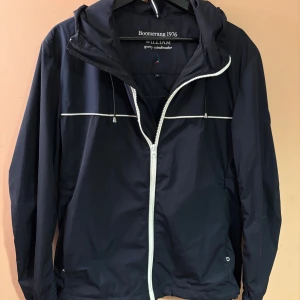 Windbreaker från Boomerang - .Snygg mörkblå vindjacka från Boomerang med vit dragkedja och vita detaljer över bröstet och ryggen. Jackan har huva med snörning och sportig look. Perfekt för blåsiga dagar och enkel att matcha med jeans eller joggers. Nypris: 2299. Skick 10/10 ☺️