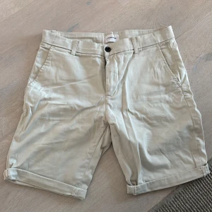 Beige shorts från Lindbergh - Snygga beige shorts från Lindbergh med klassisk passform. De har uppvikta benslut, bälteshällor, sidofickor och bakfickor med knapp. Perfekta för varma dagar och lätta att matcha med det mesta. Materialet är mjuk bomull.