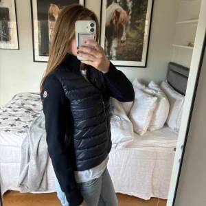 Moncler Cardigan Padded Wool Zip-Up  - Säljer min marinblå Padded Wool Zip-Up Cardigan från Moncler med stickade ärmar och quiltad framsida. Jackan har en hög krage, dragkedja framtill och vit Moncler-logga på ärmen. Använts fåtal gånger men säljer då den inte kommer till användning. Äktighetsbevis tillkommer, Storlek S!
