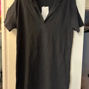 Svart kortklänning/tunika från Zara, stl L - Svart kortklänning från Zara i storlek L. Klänningen har en enkel och stilren design med korta ärmar och en liten krage med v-ringad öppning. Materialet är mjukt och känns bekvämt mot huden, perfekt för en chill och snygg look. 