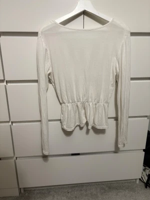 Vit omlottopp - Säljer en vit långärmad omlottopp med v-ringning och volang nedtill. Toppen har en fin passform och bara använd några få ggr. Vet varken storlek eller märke men skulle säga att den passar någon med ungefär storlek XS/S.