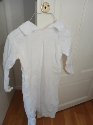 Vit långklänning med krage - Säljer en vit långklänning med klassisk krage och långa ärmar. Klänningen har en rak och enkel design utan mönster eller detaljer, perfekt för dig som gillar minimalistisk stil. Materialet känns lätt och luftigt, passar bra till varmare dagar.