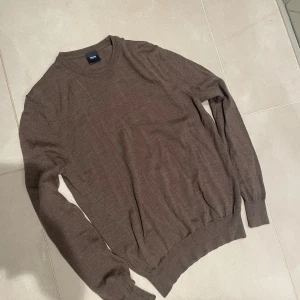 Brun stickad tröja från adverb - Snygg brun stickad tröja från adverb med rund hals och långa ärmar. Tröjan har ribbade muddar vid ärmslut och nederkant, perfekt för att hålla värmen under kyliga dagar. Enkel och stilren design som passar till många olika outfits.