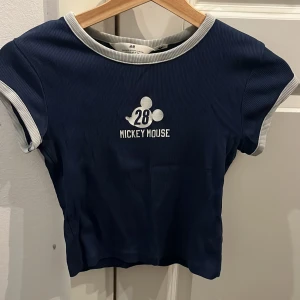 Blå topp - En blå topp med vitt/grått på kanterna och en fin mickey mouse print i mitten. Har andvänt mycket men går forfarande att andvända. Står inte storlek!! Men är mellan 10-12!! Fast lite liten i storlek 