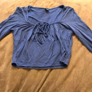 Blå långärmad topp med knyt - Säljer en blå långärmad topp med snygg knytning framtill och rundad hals. Modellen är croppad och har en mjuk, lätt känsla i materialet. Perfekt att styla med jeans eller kjol för en chill look. Pris kan diskuteras och köparen står för frakt