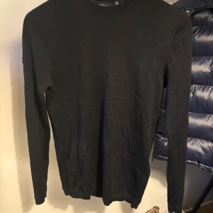 Svart merinotröja från Superdry - Svart långärmad tröja från Superdry i 100% fin merinoull. Enkel och stilren design med rund hals och diskret Superdry-logga på ärmen. Perfekt för dig som gillar klassiska och bekväma plagg med lite lyxigare känsla. (loggan på armen går enkelt att sprätta bort om man skulle vilja)