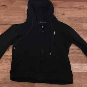 Ralph lauren zip svart - Helt oanvänd med tags kvar, Svart hoodie från Polo Ralph Lauren med vit broderad logga på bröstet. Tröjan har huva med snörning, dragkedja framtill och Perfekt för chill dagar och streetwear-stil. 